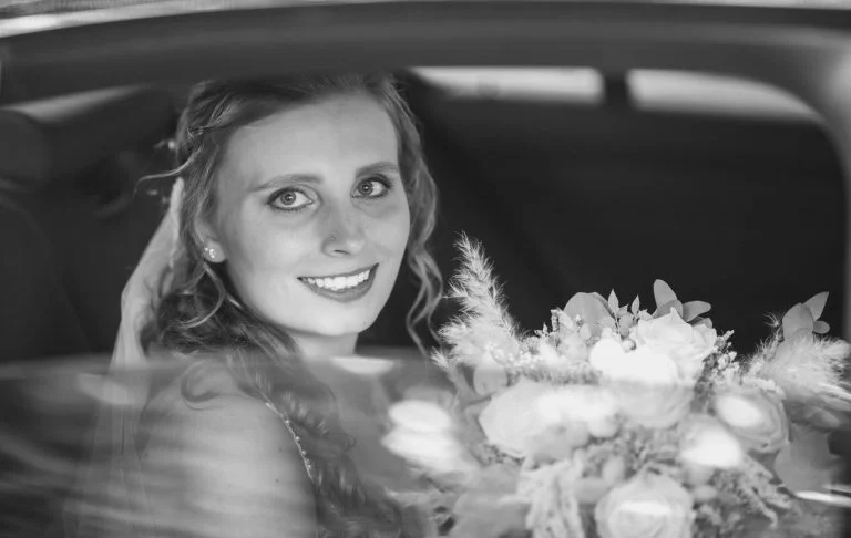 Hochzeit Bad Driburg Braut lächelt im Auto mit einem Blumenstrauß in der Hand.