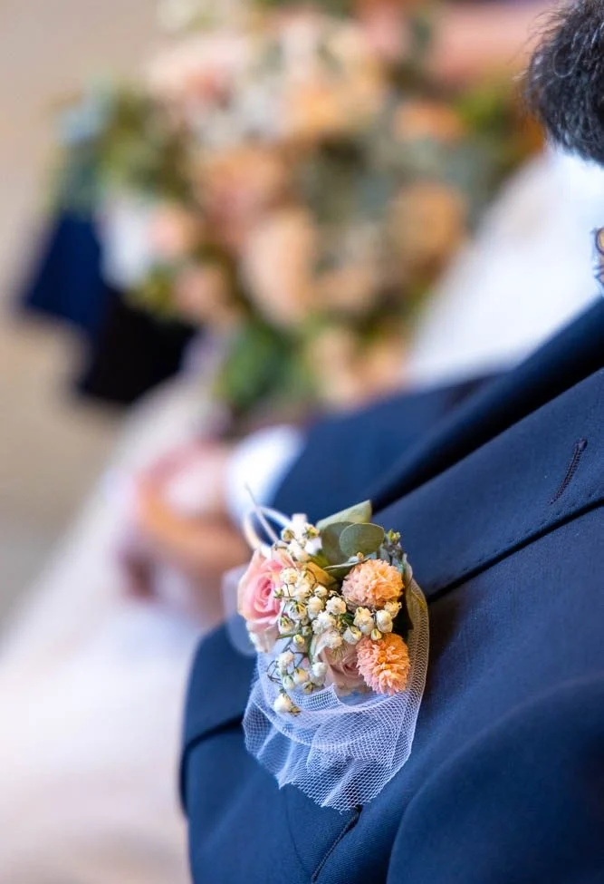 Hochzeitsfotograf Bad Driburg Ansteckblume mit kleinen Blumen und Grün auf dem Jackett eines Bräutigams gekleideten Mannes.