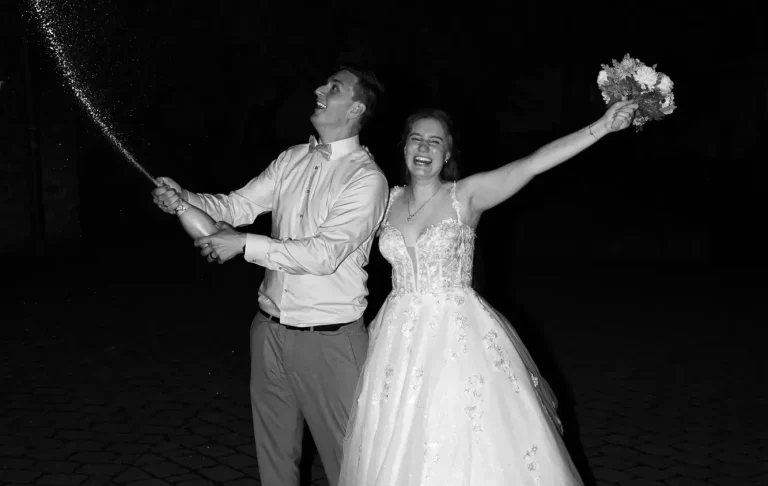 Hochzeitsfotograf Bad Driburg Ein Brautpaar feiert mit Sekt und einem Strauß vor nächtlicher Kulisse.