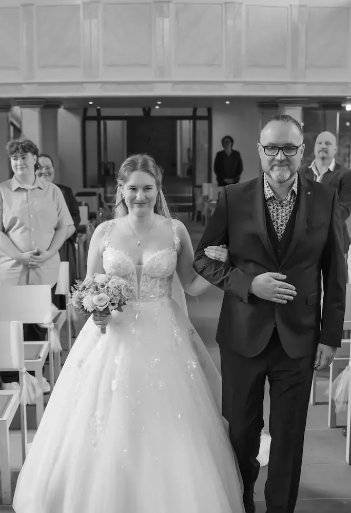 Hochzeitsfotograf Bad Driburg Braut mit Blumenstrauß, arm in arm mit ihrem Vater, geht den Gang entlang.